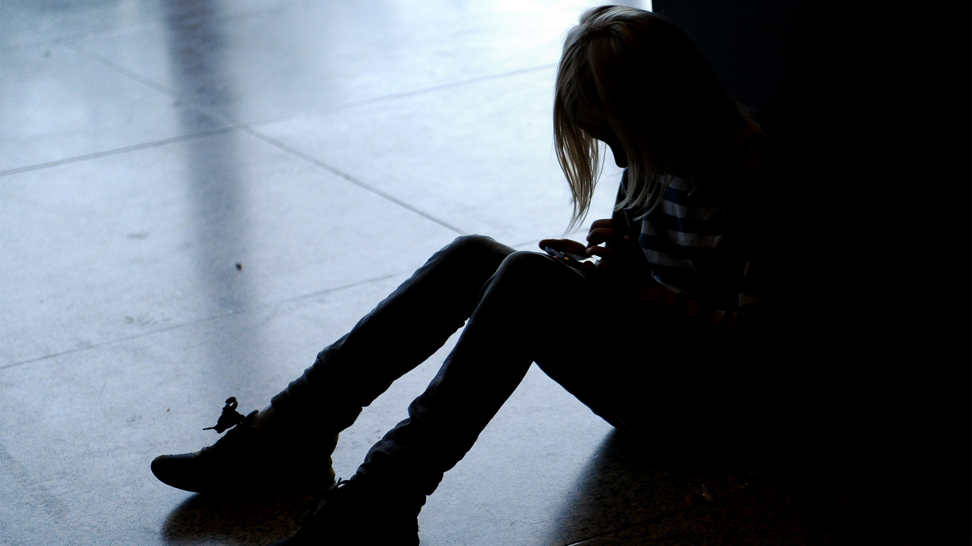 Ein Mädchen sitzt mit gesenktem Kopf allein auf dem Fußboden.  | picture alliance/dpa/dpa-Zentral